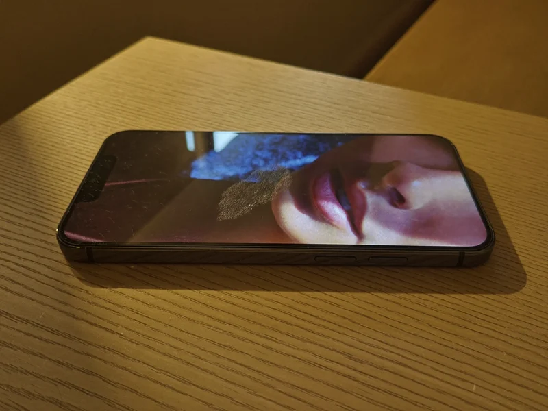 Illustration af en slank smartphone med mørk glasbagside på et egetræsbord
